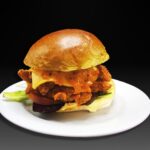 Hamburguesa Crispy, Pollo crujiente empanado, lechuga, tomate, cebolla, ali-oli, queso checar y salsa emi (un toque picante)