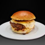 Hamburguesa Inglesa, Bacon tostado crujiente, doble de queso edam derretido, tomate natural a la plancha, pepinillo laminado y cebolla frita con salsa de boletus